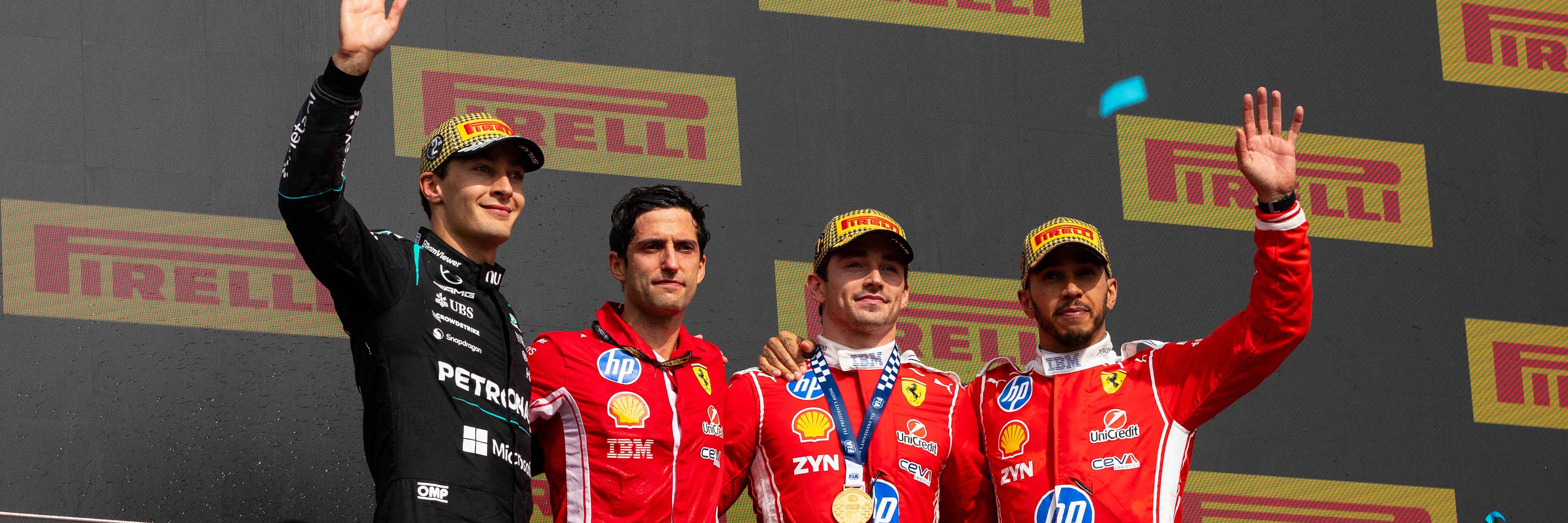 Four Formula 1 drivers stand on a winners' podium, waving to the crowd; Pirelli banners in the background (gray backdrop).